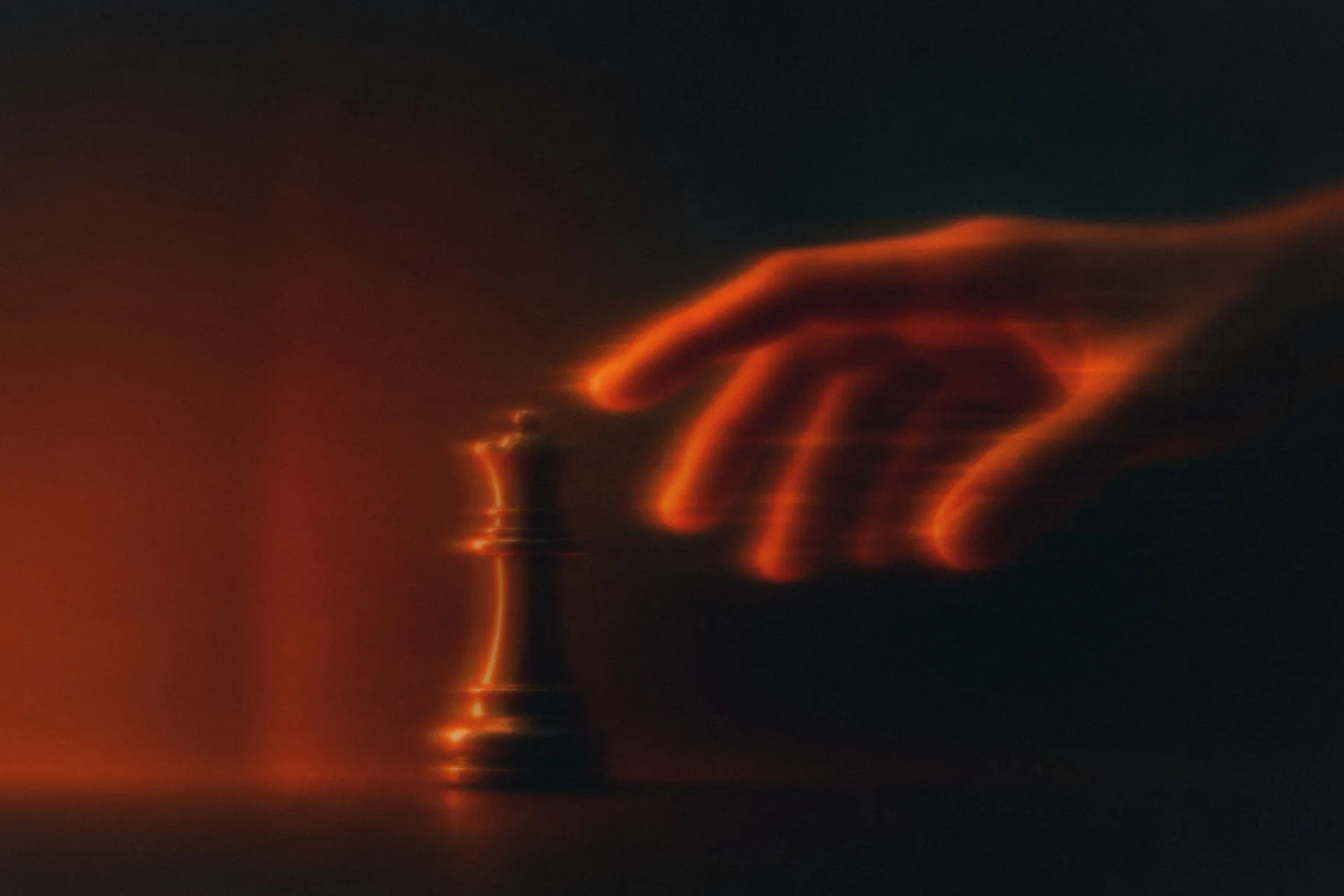 A hand about to pick up the chess queen, lit in orange on a dark background